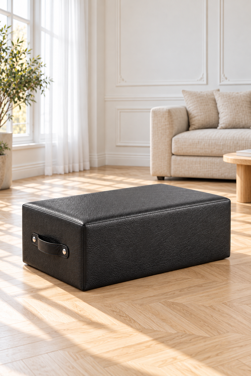 Box Pilates noire au dessus rembourré, avec sa poignée, posée sur un parquet dans un salon lumineux