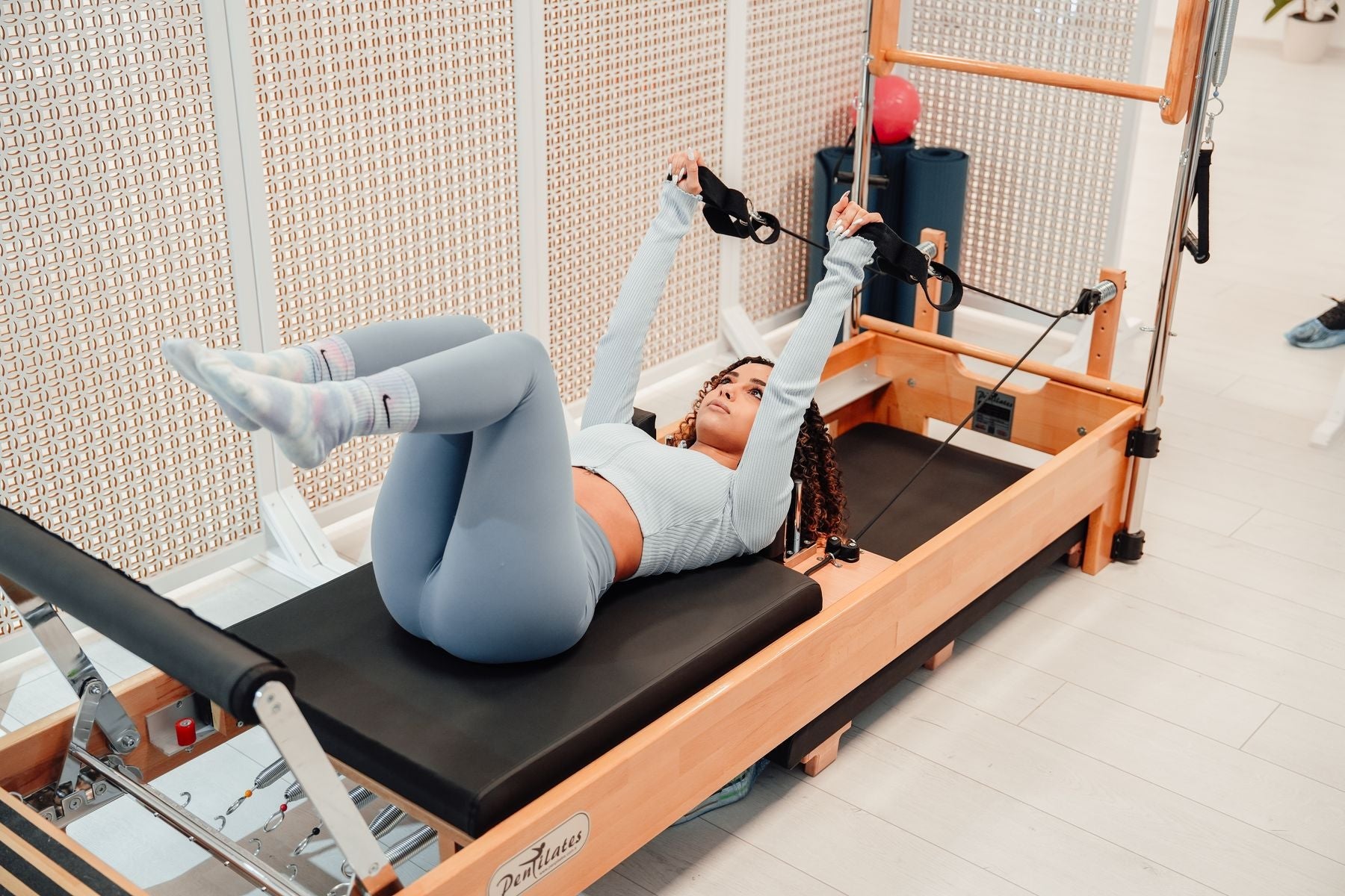 Une femme fait du Pilates allongée sur un reformer en bois