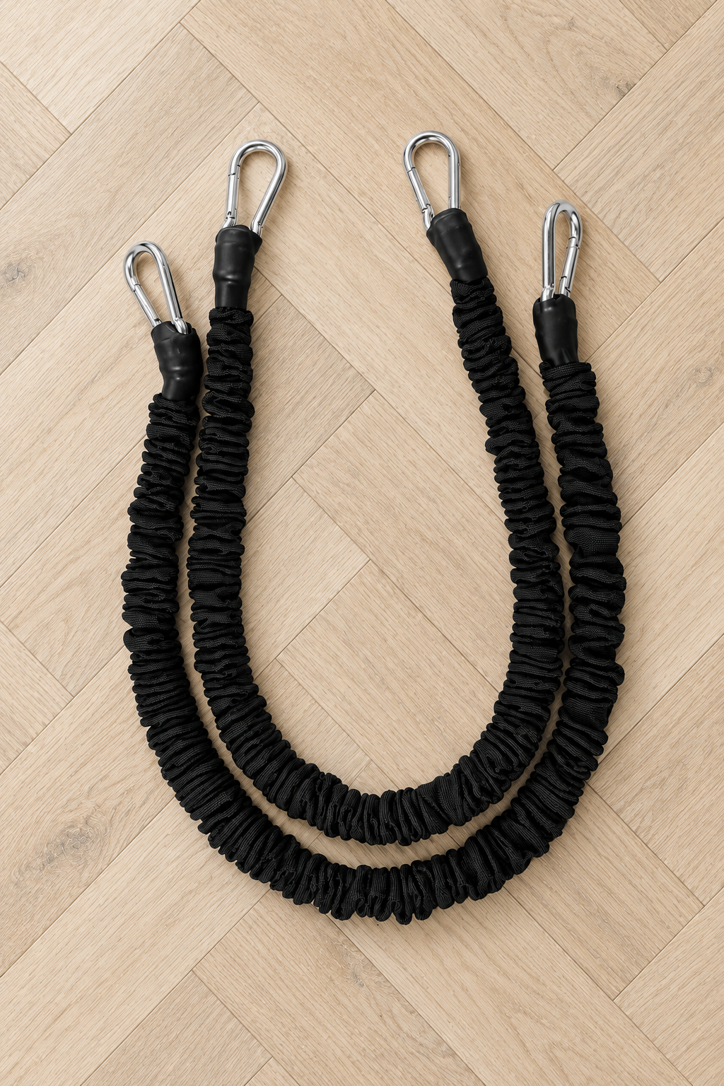 Deux élastiques de résistance noirs avec mousquetons en acier, posés sur un parquet